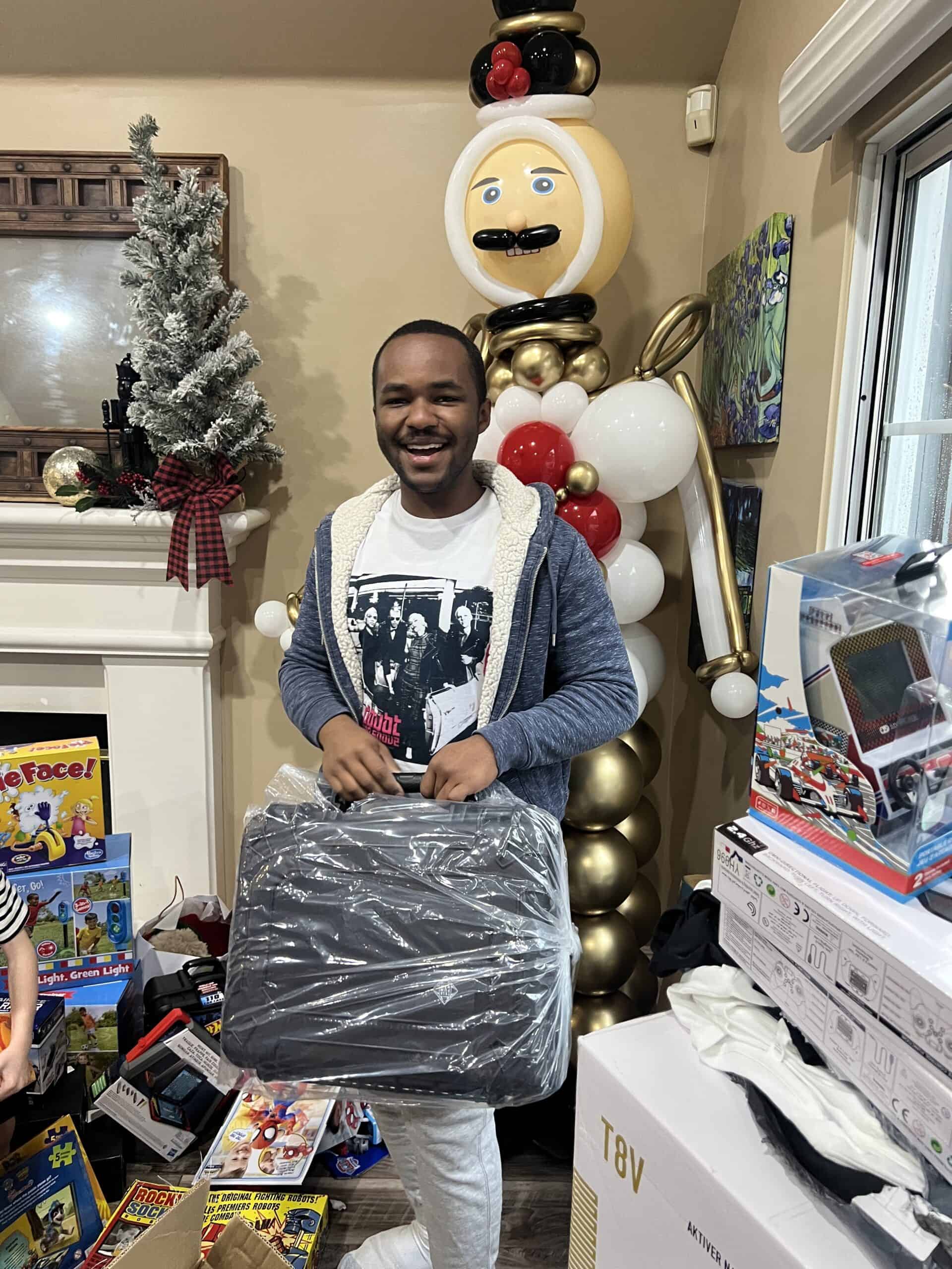 Happy young man at Loving Hands Children's Home surrounded by toys and holiday decorations, celebrating generosity and community support during festive season.